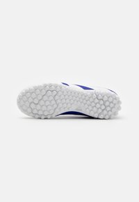 Suela de zapatilla deportiva blanca con un patrón de tracción hexagonal, con acentos de diseño y detalles de logo en azul. Textura de goma suave observada.