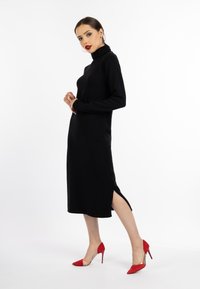 Zwarte midi-jurk met col en zijsplitten, gemaakt van zachte stof. Gecombineerd met rode suède high heels. Strak, minimalistisch ontwerp.