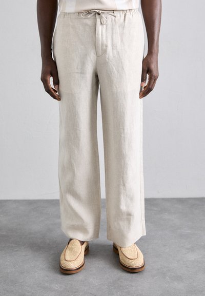 Pantalons en lin beige clair à coupe décontractée, dotés d'une taille élastique avec cordon de serrage, de poches latérales et d'une texture lisse. Associés à des chaussures à enfiler en tissu tissé.