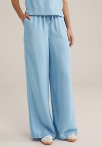 Ljusblå vida byxor i denim, med elastisk midja och snörning, samt fickor. Avslappnad och bekväm passform.