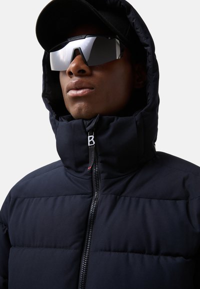 Námořnická puffer bunda s vysokým límcem, zapínáním na zip a logem BOGNER. Disponuje hladkým povrchem a elegantním designem. Nositě s tmavými slunečn�ími brýlemi.