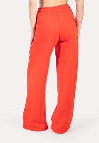 Rote Jogginghose aus weichem Material, mit weitem Bein und elastischem Bund. Helle Textur ohne sichtbare Muster.