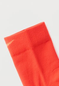 Κόκκινη αθλητική κάλτσα με ριμπ μανσέτα, υφασμάτινη δομή και ενισχυμένη περιοχή δακτύλων. Διαθέτει μια μικρή διακοσμητική λεπτομέρεια σε πιο ανοιχτή απόχρωση.