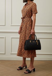 Robe-chemise imprimé léopard en orange avec manches courtes et ceinture à nouer, associée à un sac à main matelassé noir avec détails dorés et sandales plates noires.