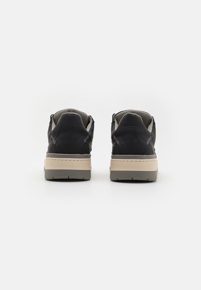 Svarta sneakers med en slät läderövre, ljusbeige mellansula och grå texturerad yttersula. Perforerade detaljer finns på baksidan.