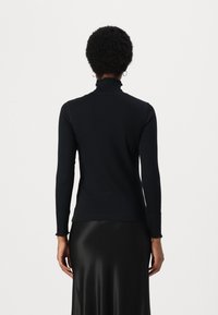 Black long-sleeve turtleneck top made of smooth, stretchy fabric with a ruffled neckline and fitted cut, paired with a flowing black skirt.