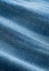 Primer plano de un tejido de denim azul texturizado con un patrón de tejido diagonal visible y suaves pliegues que crean sombras suaves.