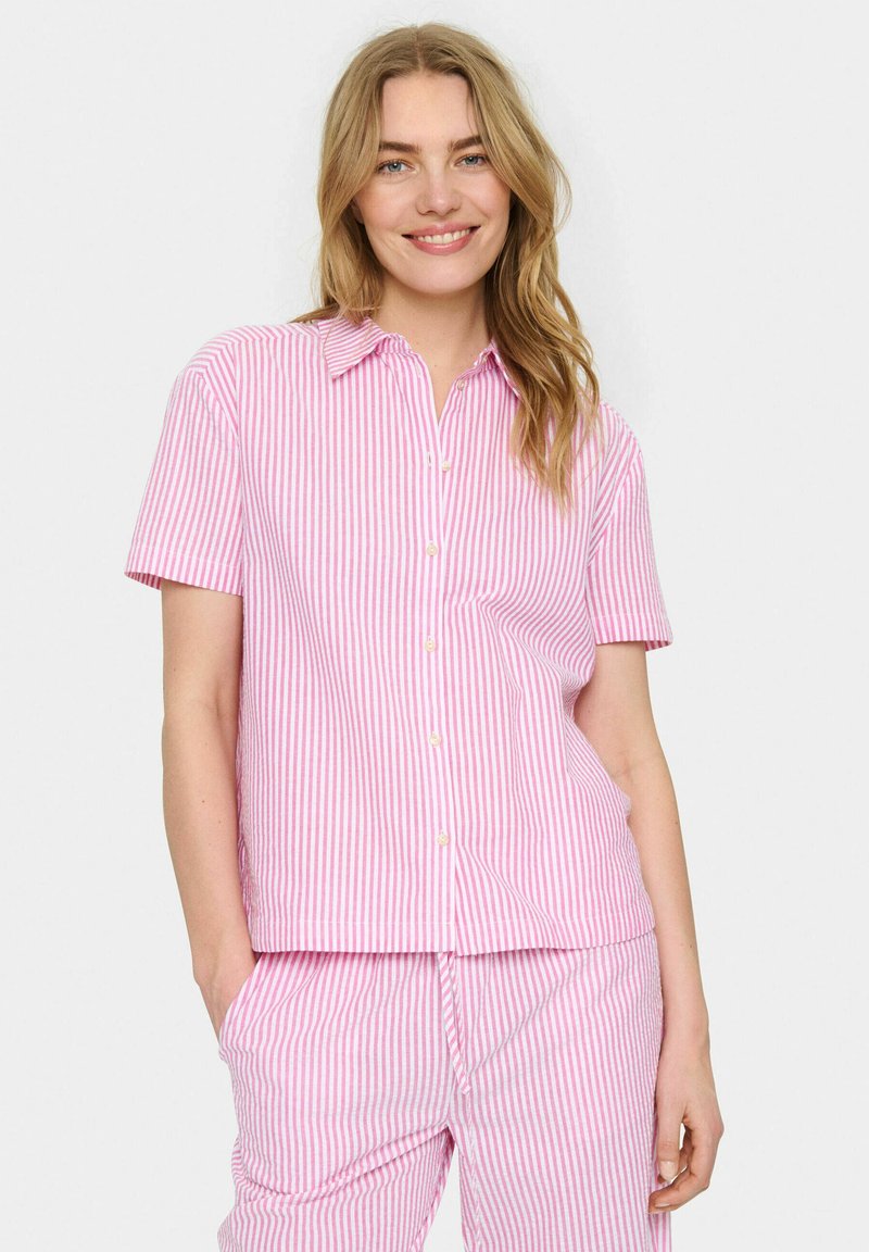 Camisa de manga corta con cuello, hecha de tela a rayas rosa y blanca. Presenta botones en la parte delantera y un ajuste relajado.