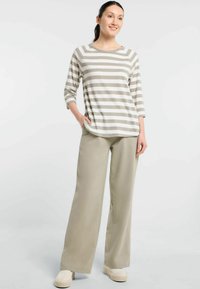 Gestreiftes Langarmoberteil in Beige und Weiß, kombiniert mit beigen weiten Hosen. Das Outfit zeichnet sich durch eine lockere Passform und einen lässigen Stil aus.