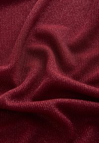 Bourgognefarvet ribbet stof med en subtil glans. Teksturen er blød med fine lodrette striber, der fremhæver dets strækbare og lette egenskaber.