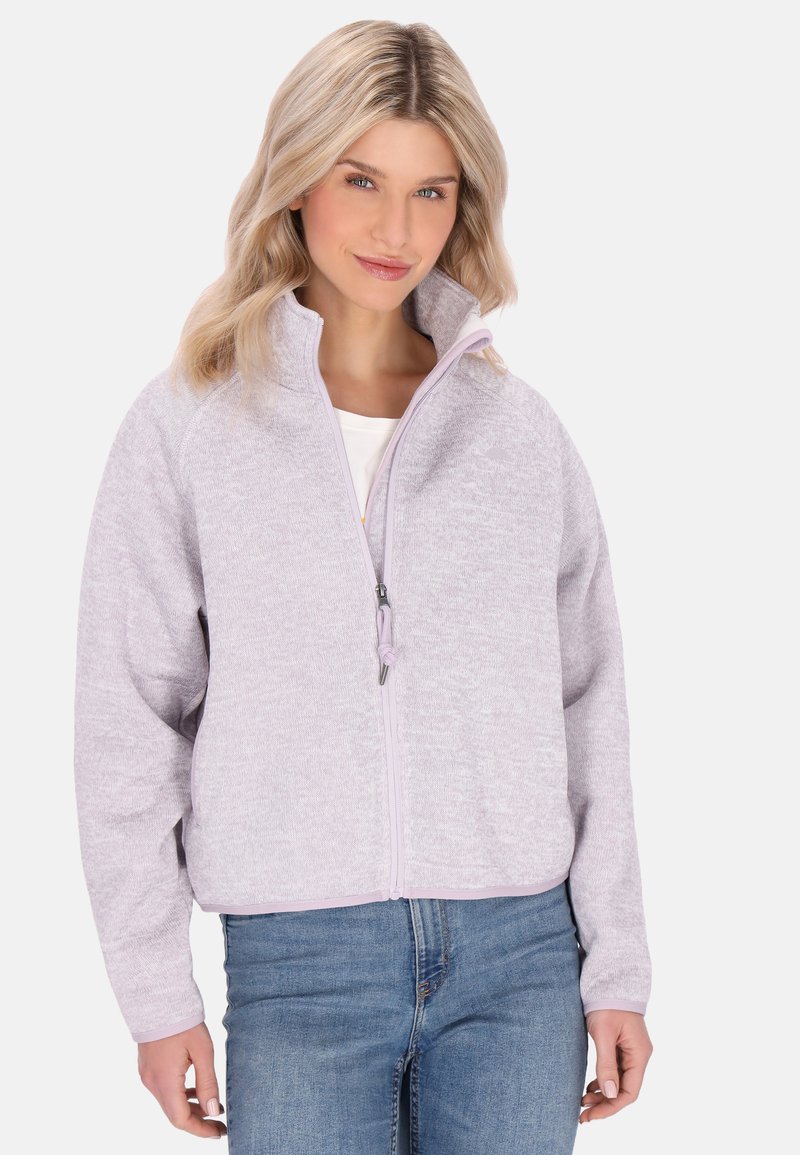 Giacca zip-up lilla chiaro con un tessuto texturizzato, colletto alto e un design bicolore. Indossata sopra una camicia bianca con jeans blu.