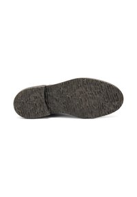 Suola di una scarpa nera che mostra una superficie testo e rude, progettata per trazione e durata, posizionata su uno sfondo bianco uniforme.