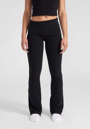 Leggings neri aderenti con fondo svasato e vita alta, realizzati in tessuto elasticizzato. Abbinati a un top corto coordinato.