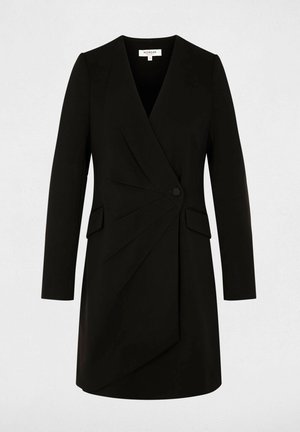 Abito nero su misura con design avvolgente, maniche lunghe, leggere pieghe e chiusura con bottoni frontali. Presenta due tasche laterali.