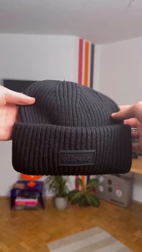 Fekete kötött sapka bordás mintával, hajtókás szegéllyel és az elején fekete, téglalap alakú logófolttal.