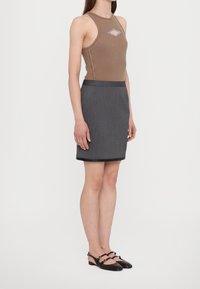 Donna che indossa un top senza maniche marrone con una scollatura frontale, una gonna grigia a righe sottili e scarpe basse nere con doppie cinghie.