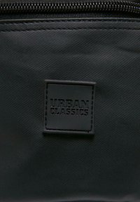 Borsa rettangolare nera con superficie testurizzata e chiusura a zip. Presenta un logo nero in rilievo con la scritta "URBAN CLASSICS" su una toppa.