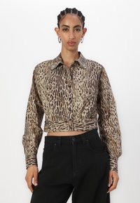 Zkrácená košile na knoflíky z látky s leopardím potiskem, s límcem s kovovými akcenty, dlouhými rukávy a černými knoflíky. V kombinaci s černými kalhotami.