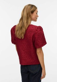 Rød tekstureret top med kort, puffet ærme, der har en boxy silhuet og et subtilt krøllemønster. Stylet med mørk denim jeans.