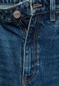 Jean en denim avec un lavage bleu, braguette zippée avec matériel métallique, et surpiqûres contrastées le long des coutures et des poches.