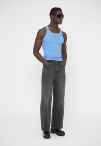 Blå linne, grå vida jeans och svarta platåstövlar. Mjukt tyg och modern design. Accessoarer inkluderar stora solglasögon.