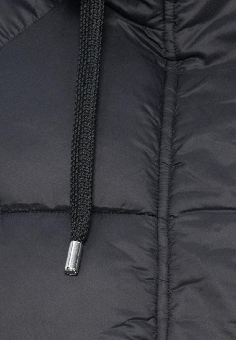 Schwarze Pufferjacke im Detail mit strukturierter Außenschale, gewebtem Kordelzug und silberner Hardware-Akzent am Kabel.