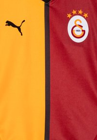 Maglia da calcio con un design diviso: giallo da un lato, bordeaux dall'altro. Presenta un logo Puma nero e uno scudetto circolare della squadra con tre stelle.