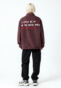 Pull polaire bordeaux avec texte blanc et rouge au dos. Associé à un pantalon cargo noir et des baskets blanches, avec des poignets élastiques.