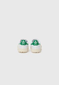 White sneakers with green accents, featuring a textured sole, smooth leather upper, and embossed logo on the heel.
