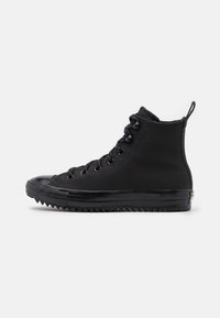 Zapatillas altas negras de lona, con una puntera de goma y suelas texturizadas con un patrón en zigzag, equipadas con ojales negros.