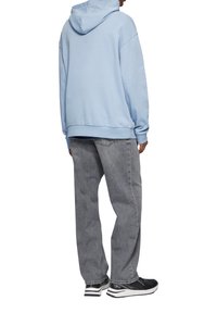 Lichtblauwe capuchontrui met een relaxte pasvorm, gecombineerd met losse grijze spijkerbroek en zwarte sneakers met witte accenten.