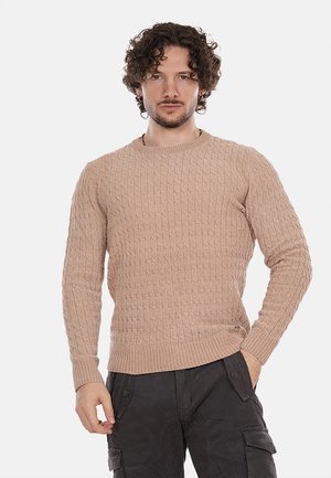 Maglione beige a maglia testurizzata con scollatura rotonda e orlo a coste. Presenta un motivo a nido d'ape e maniche lunghe. Abbinato a pantaloni scuri.