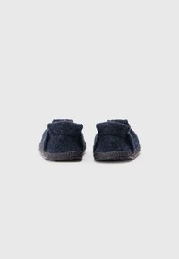 Zapatillas de casa de color navy con una textura suave, parte trasera redondeada y suela de goma gris. Presentan un diseño minimalista y un borde doblado en la parte superior.