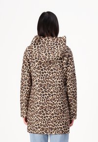 Leopard print coat with a hood, featuring a beige base and dark brown spots, mid-length, made of textured fabric, paired with light blue jeans.