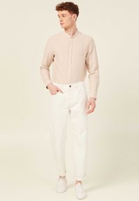 Camicetta giallo chiaro con maniche lunghe e bottoni abbinata a pantaloni bianchi a sigaretta e sneakers bianche. La camicia presenta un colletto alla band; i pantaloni hanno le maniche arrotolate.