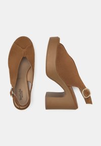 Chaussures ouvertes en daim marron avec un design à bride arrière, dotées d'un talon épais et d'un accent en boucle métallique circulaire. Texture lisse tout au long.