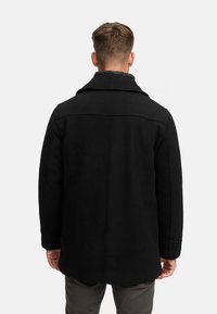 Schwarzer Wollmantel mit strukturiertem Kragen, sichtbaren Nähten und geradem Schnitt. Verfügt über einen strukturierten Stoff und eine Länge bis zur Mitte des Oberschenkels.