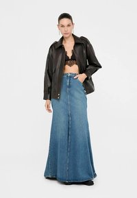 Svart lädercroppad jacka, spets-bh och lång blå jeanskjol med utsvängd nederkant. Modellen står mot en enfärgad vit bakgrund.