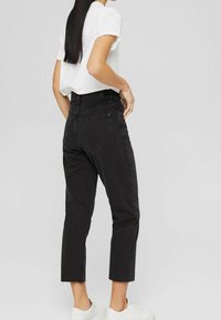 Vaqueros de denim negros cortos con cintura alta, cinco bolsillos y dobladillos deshilachados, combinados con una camiseta blanca de manga corta y zapatillas blancas.