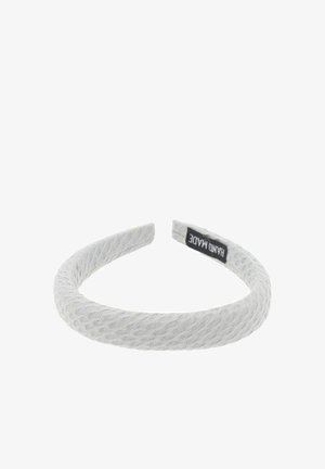 Teksturowana, elastyczna opaska na głowę w jasnoszarym kolorze z plecionym wzorem. Z boku znajduje się czarna metka z napisem "HANDMADE". Okrągły kształt.