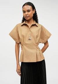 Κοντομάνικο καρό πουκάμισο σε καφέ βαμβάκι με δομητή εφαρμογή, διαθέτει ασημένια λεπτομέρεια και κουμπωτή λαιμόκοψη.