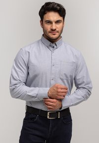 Jasnoszara koszula z kołnierzykiem, kieszenią na piersi i długimi rękawami, uszyta z teksturowanej tkaniny, zestawiona z ciemnymi dżinsami i czarnym paskiem.