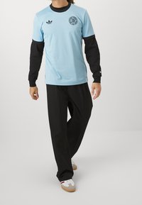 Ljusblå kortärmad skjorta med svarta accenter och logotyp, lager på en svart långärmad skjorta. Kombineras med löst sittande svarta byxor och sneakers.