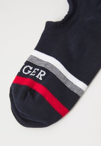 Chaussette de cheville bleu marine avec des rayures blanches et rouges, comportant le mot "TOMMY" en lettres blanches sur une bande rayée. Texture tricotée douce.
