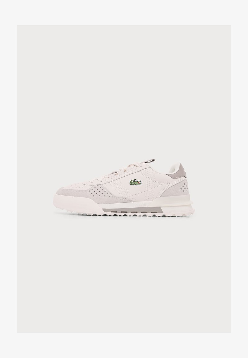 Baskets basses blanches et gris clair avec lacets à l’avant et logo crocodile vert sur le côté, présentées sur un fond clair uni.