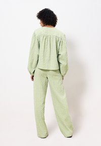 Groene ruitjes, losvallend bovenstuk met pofmouwen en wijde broek. Katoenen stof met een lichte textuur. Achteraanzicht.