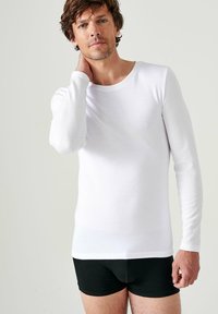 Witte langemouwige shirt gemaakt van gladde stof, met een ronde halslijn en een getailleerd ontwerp. Draag het met zwarte shorts, eenvoudige textuur.