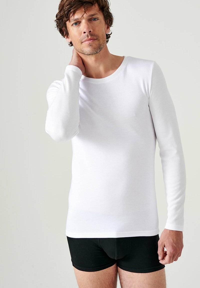 Witte langemouwige shirt gemaakt van gladde stof, met een ronde halslijn en een getailleerd ontwerp. Draag het met zwarte shorts, eenvoudige textuur.