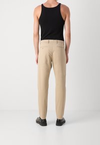 Pantaloni beige con una texture liscia, caratterizzati da una vestibilità slim e tasche posteriori. Abbinati a una canotta nera e scarpe nere.