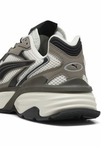 Baskets sportives avec mesh blanc, accents en cuir gris et noir, semelle blanche épaisse et logo Puma au talon arrière.